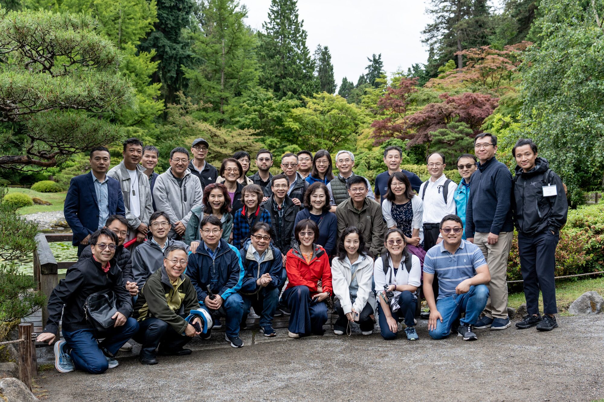 A group of investigators, some kneeling in front, on a garden path under maple trees.