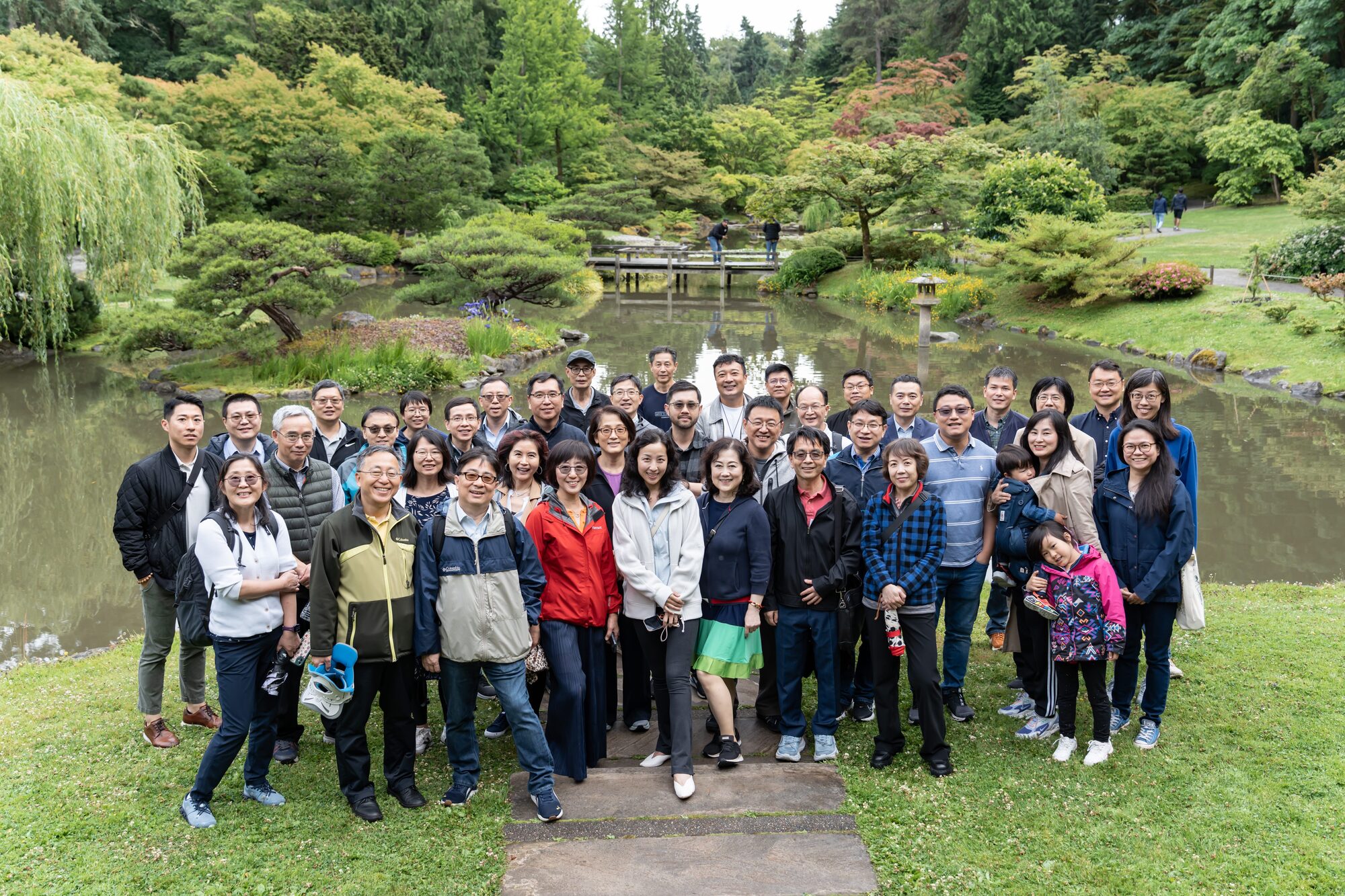 About forty investigators stand together on a lawn beside a pond in a Japanese garden.